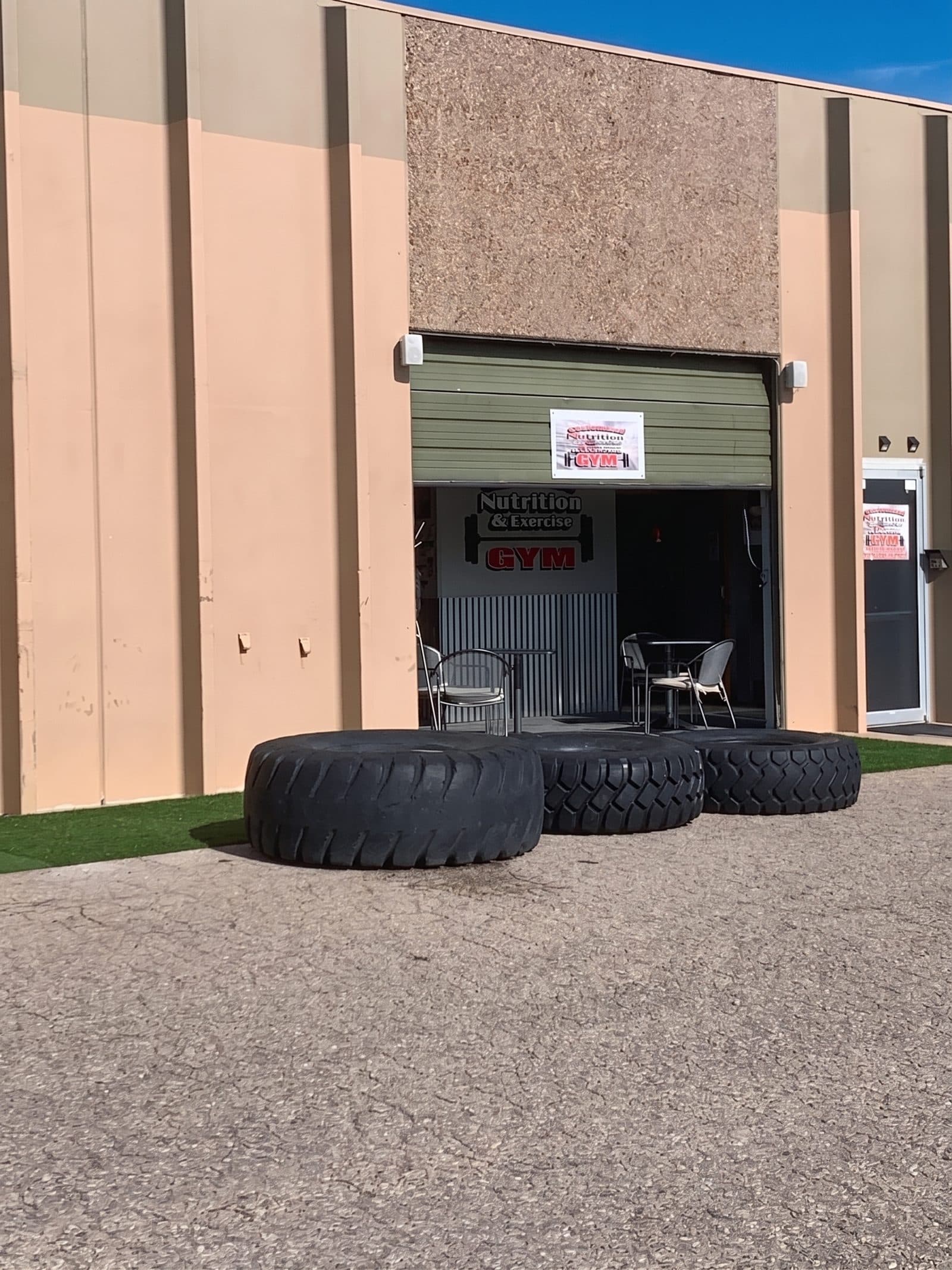 The entrance to CNE on Pearl Street: an open roll-up door under the Customized Nutrition & Exercise Gym sign, with three tractor tyres and a patch of turf out front