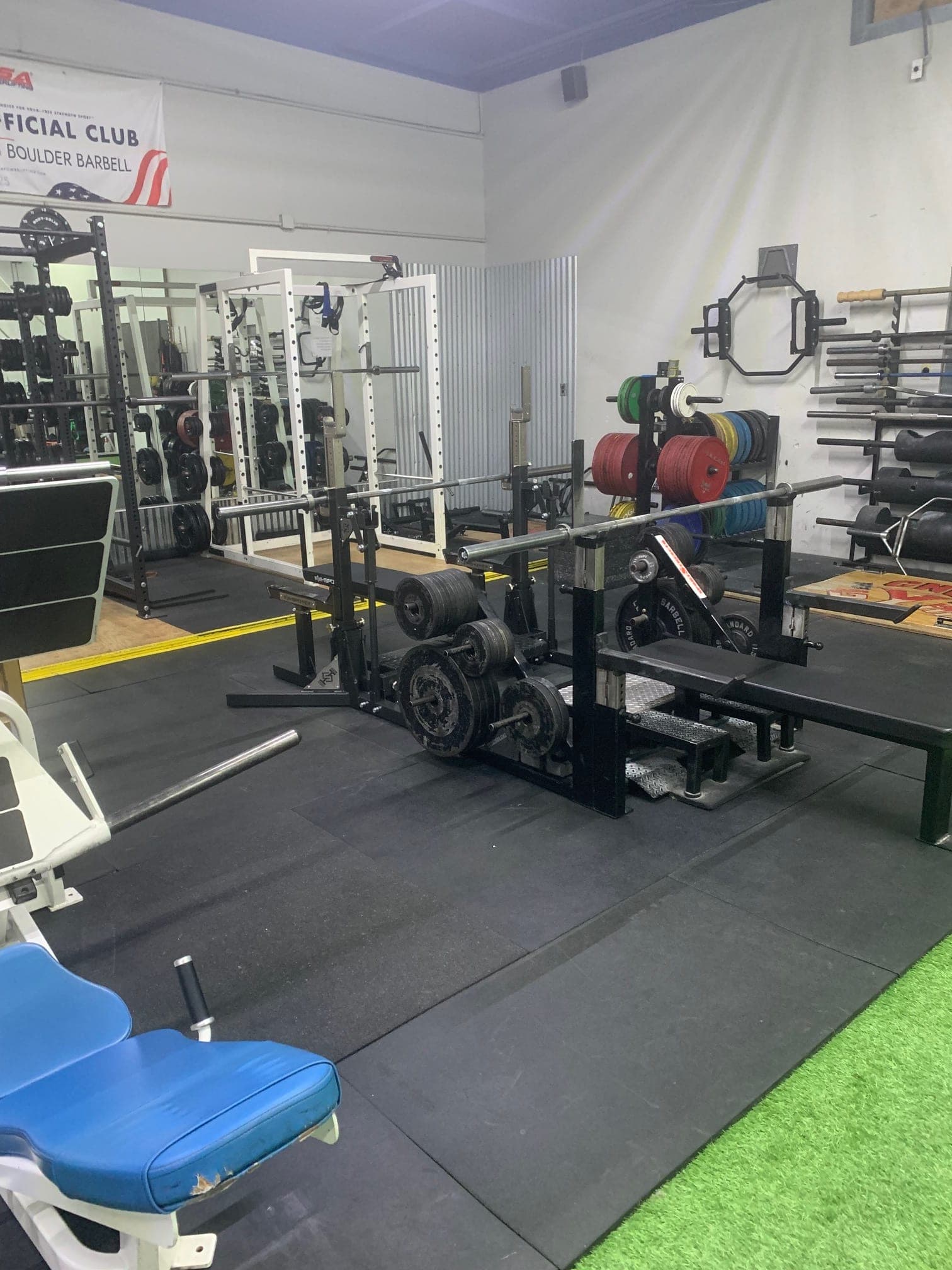 CNE's strength floor: deadlift platforms, racked barbells, and color bumper plates beside the turf lane